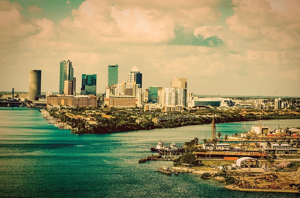 Iconic Florida 5 A wide view of Tampa Bay's skyline. You can see water and a skyline of tall buildings in the background.