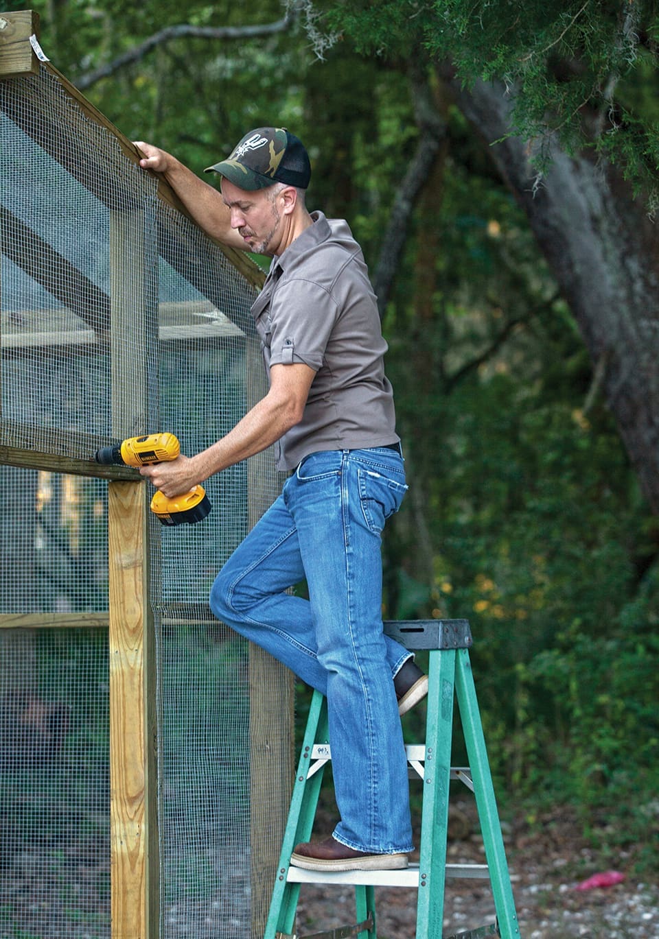 Red, White and JJ GREY 5 JJ Grey wears a camo baseball cap, gray sport polo and blue jeans while he climbs on a stepladder to drill in something on his chicken coop.
