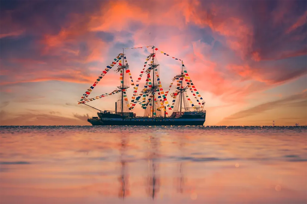 A pirate ship sailing at sunset.